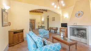 A living room with a fireplace, wooden furniture, and a TV. - Apartment 'La Terrazza' with Shared Pool, Private Terrace & Wi-Fi (Montespertoli)