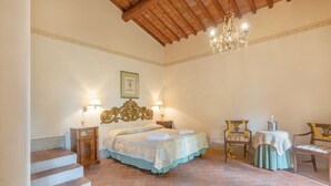 A bedroom with a bed, two nightstands, a chandelier, a chair, a small table, and a staircase. - Apartment 'La Terrazza' with Shared Pool, Private Terrace & Wi-Fi (Montespertoli)
