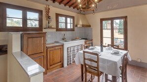A kitchen with wooden cabinets, a tiled backsplash, a dining table with chairs, and a hanging light fixture. - Apartment 'La Torre' with Shared Pool, Private Terrace & Wi-Fi (Montespertoli)