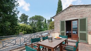 An outdoor patio with a table and chairs, a brick building with green shutters, and a stone staircase. - Apartment 'La Torre' with Shared Pool, Private Terrace & Wi-Fi (Montespertoli)