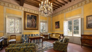 A room with a chandelier, a piano, a sofa, and a large painting on the wall. - Villa Milani with Shared Pool, Private Terrace & Wi-Fi (Montespertoli)