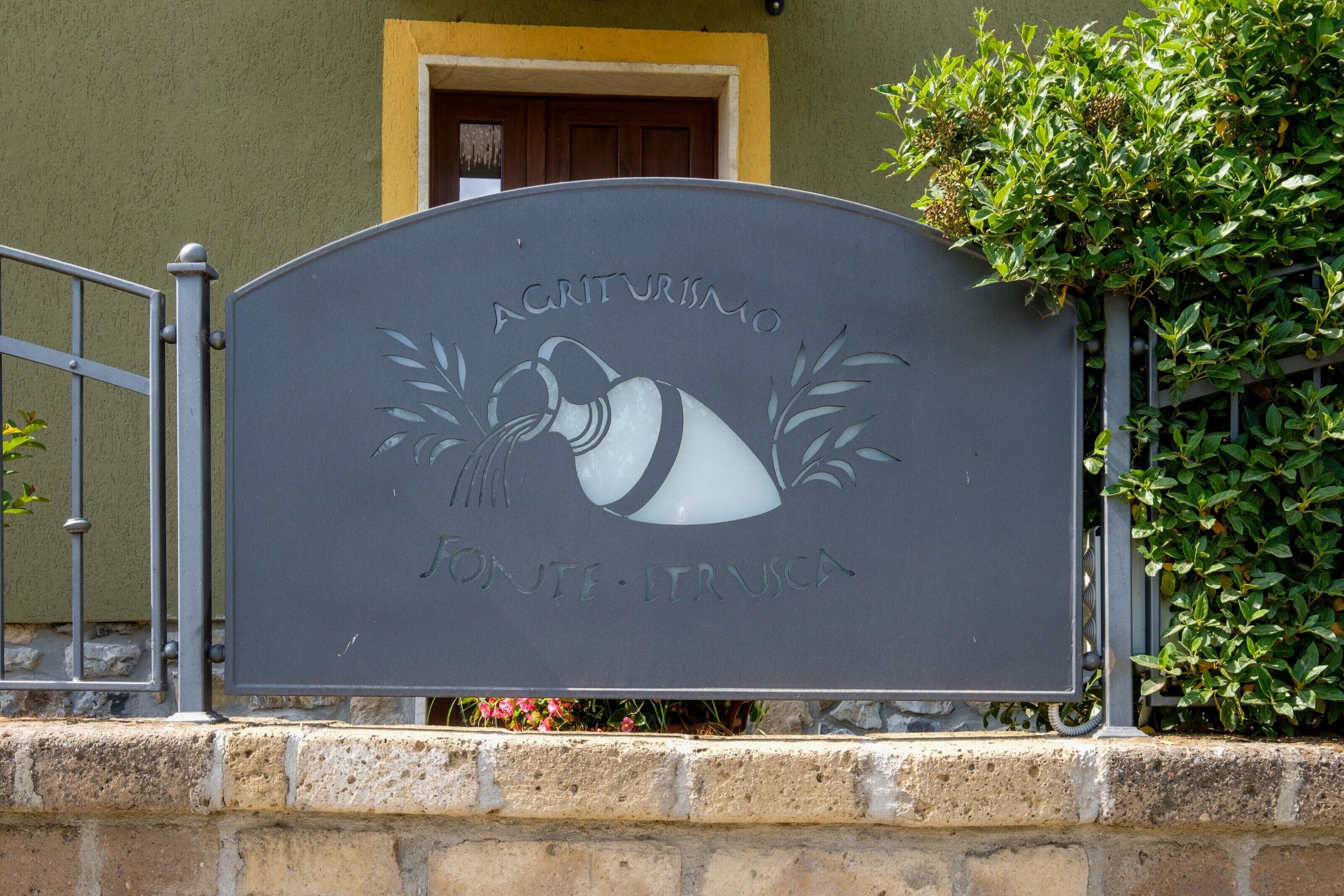 Une plaque portant les inscriptions « AGRICULTURISMO » et « FONTE - FRUSCA » est fixée à un portail en métal.