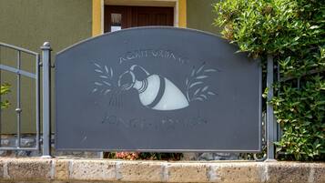 Une plaque portant les inscriptions « AGRICULTURISMO » et « FONTE - FRUSCA » est fixée à un portail en métal.