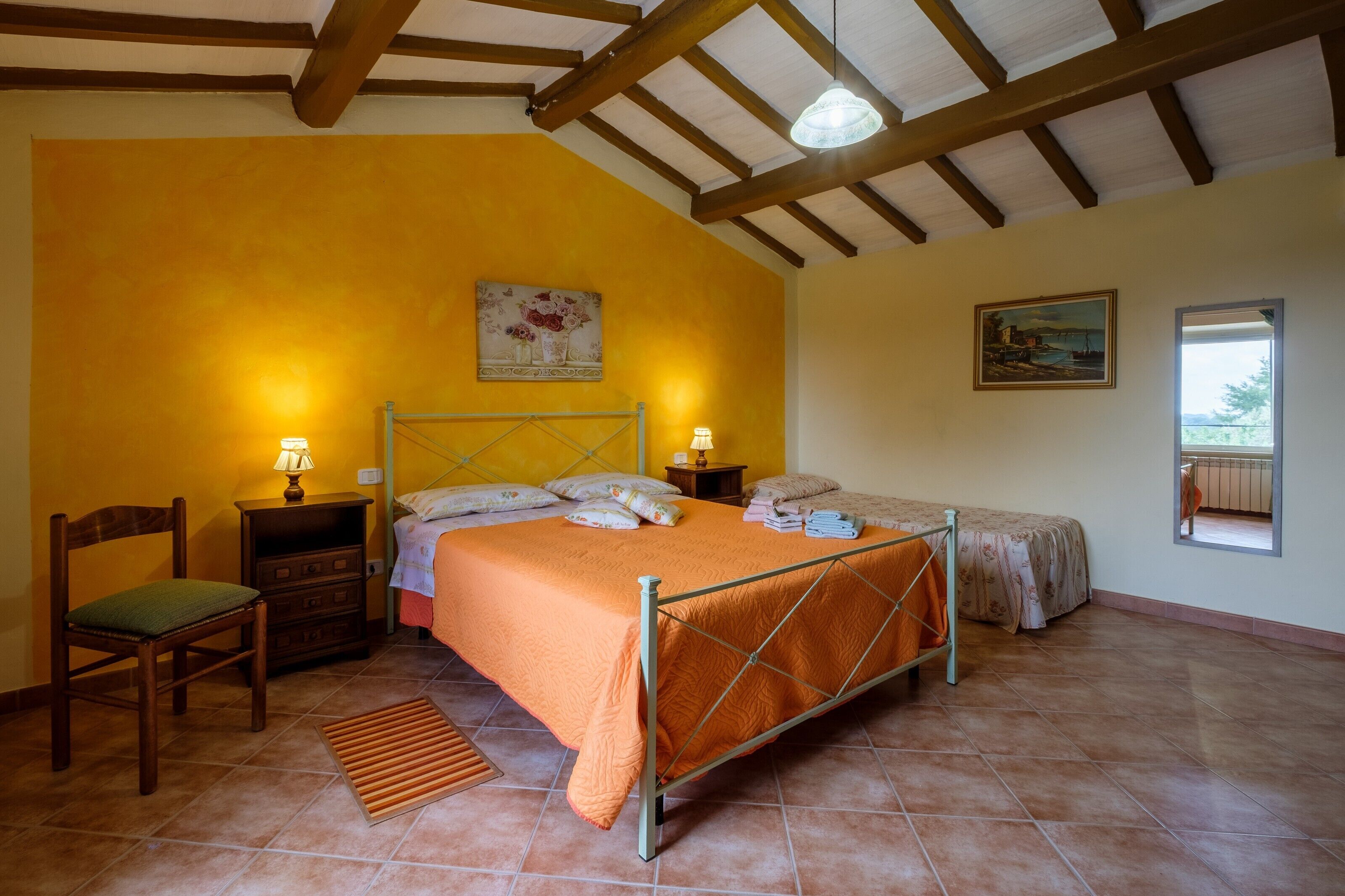 A bedroom with a bed, two bedside tables, a chair, a window, and a painting on the wall.