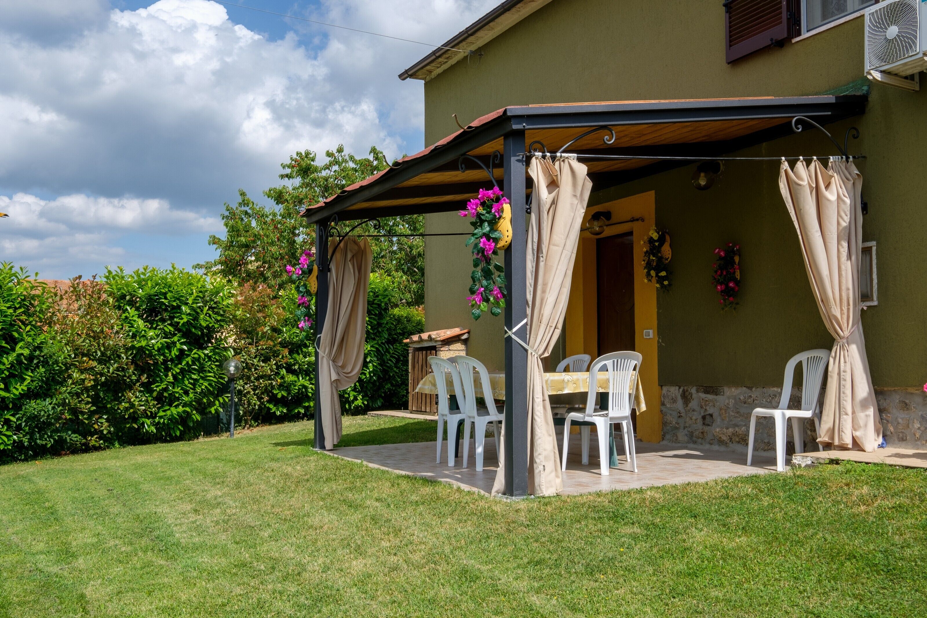 Une terrasse couverte avec une table et des chaises, un mur en pierre et un jardin.