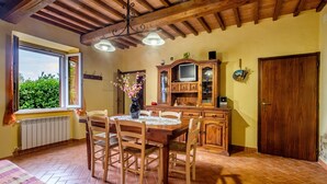 A dining area with a wooden table and chairs, a window with curtains, a radiator, and a wooden cabinet with a television. - Pet-Friendly Holiday Home Fonte Etrusca with Pool, Garden & Wi-Fi (sorano)