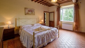 A bedroom with a bed, wooden ceiling beams, a window with curtains, a radiator, and a painting on the wall. - Pet-Friendly Holiday Home Fonte Etrusca with Pool, Garden & Wi-Fi (sorano)