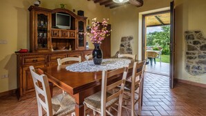 A wooden dining table with chairs, a vase with flowers, a television on a cabinet, and a stone wall. - Pet-Friendly Holiday Home Fonte Etrusca with Pool, Garden & Wi-Fi (sorano)
