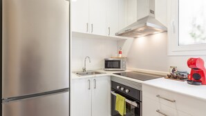 A modern kitchen with stainless steel appliances, white cabinetry, a microwave, oven, and a red coffee maker.