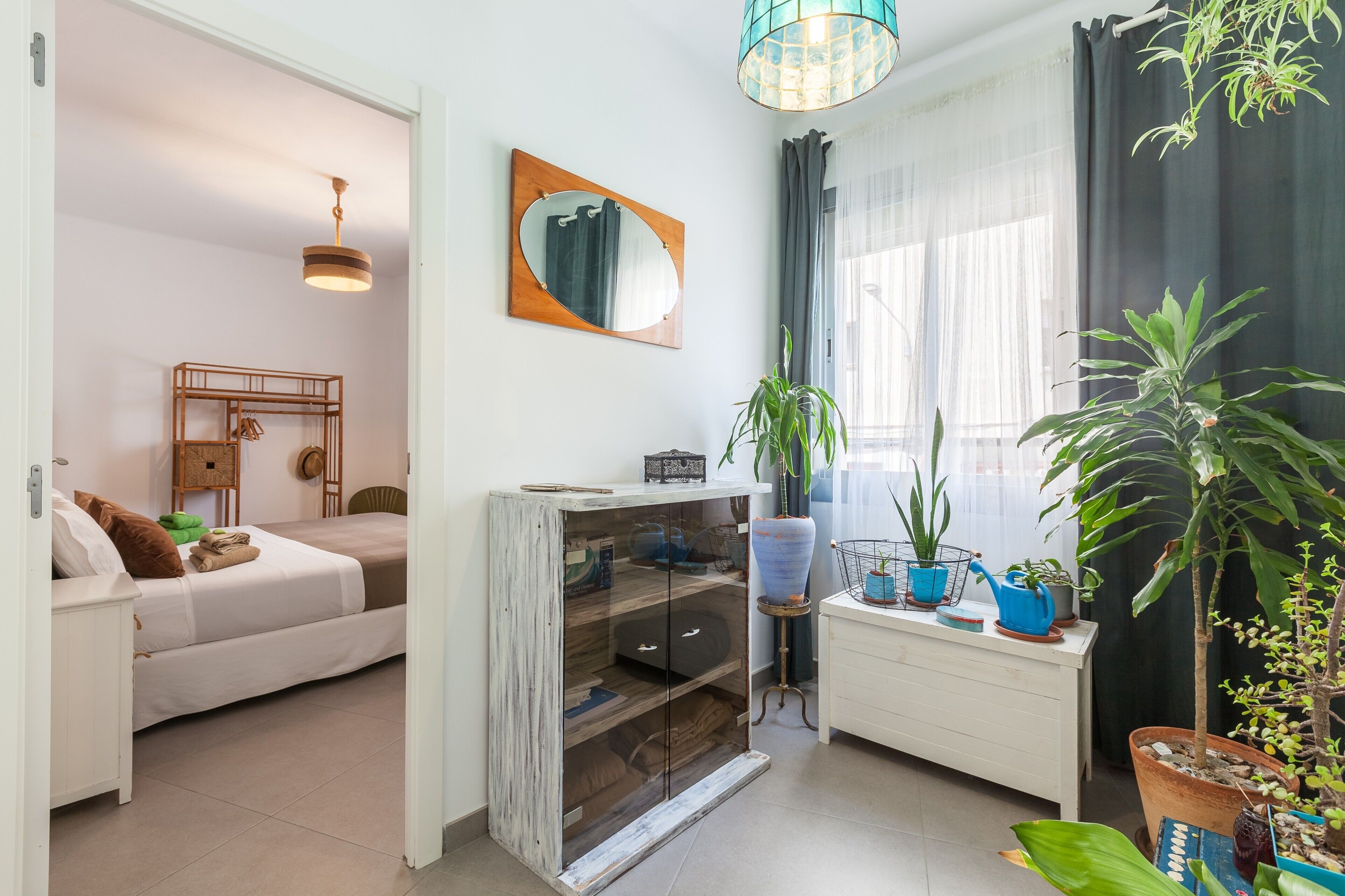 Una habitación con cama, un escritorio pequeño, un espejo y plantas en macetas.