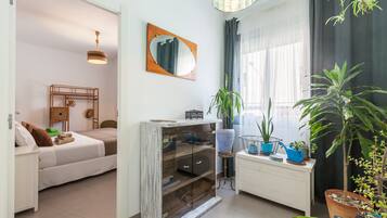 Una habitación con cama, un escritorio pequeño, un espejo y plantas en macetas.