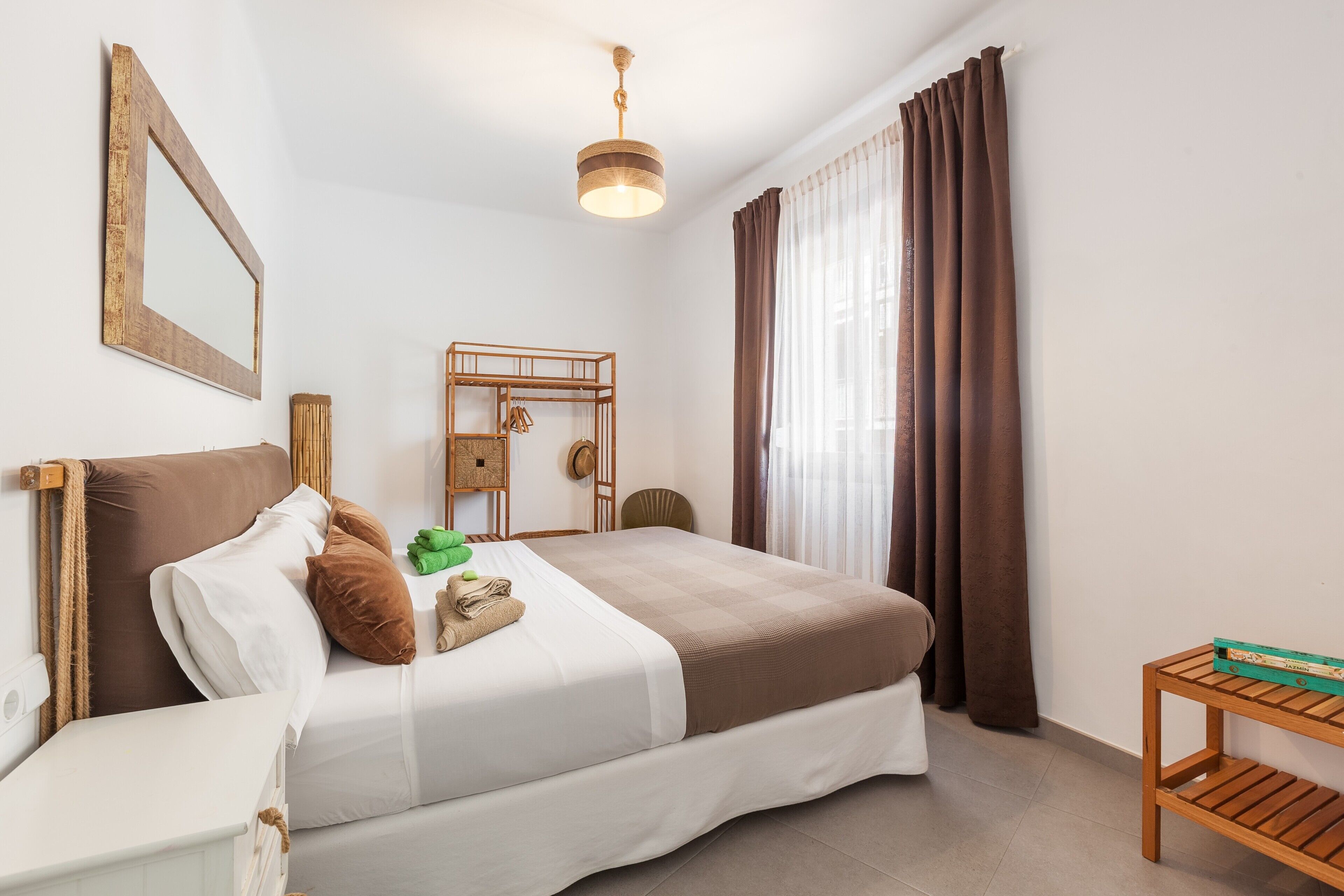 Una camera d'albergo ordinata con un letto, un comodino, uno specchio e un piccolo tavolino in legno.