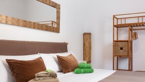 A neatly made bed with pillows and folded towels, a wooden headboard, a mirror, and a wooden shelf with a basket.