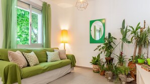 A room with a green sofa, a wall-mounted mirror, and various potted plants.