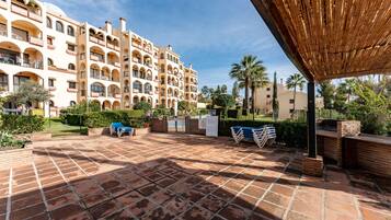 A courtyard with a tiled floor, a covered seating area, and a building with multiple balconies.