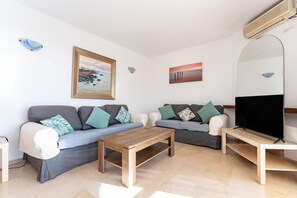 Un salon comprenant deux canapés, une table basse, un téléviseur et un climatiseur fixé au mur.