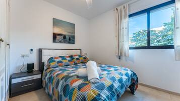 A bedroom with a bed, a nightstand, a painting, and a window with curtains.