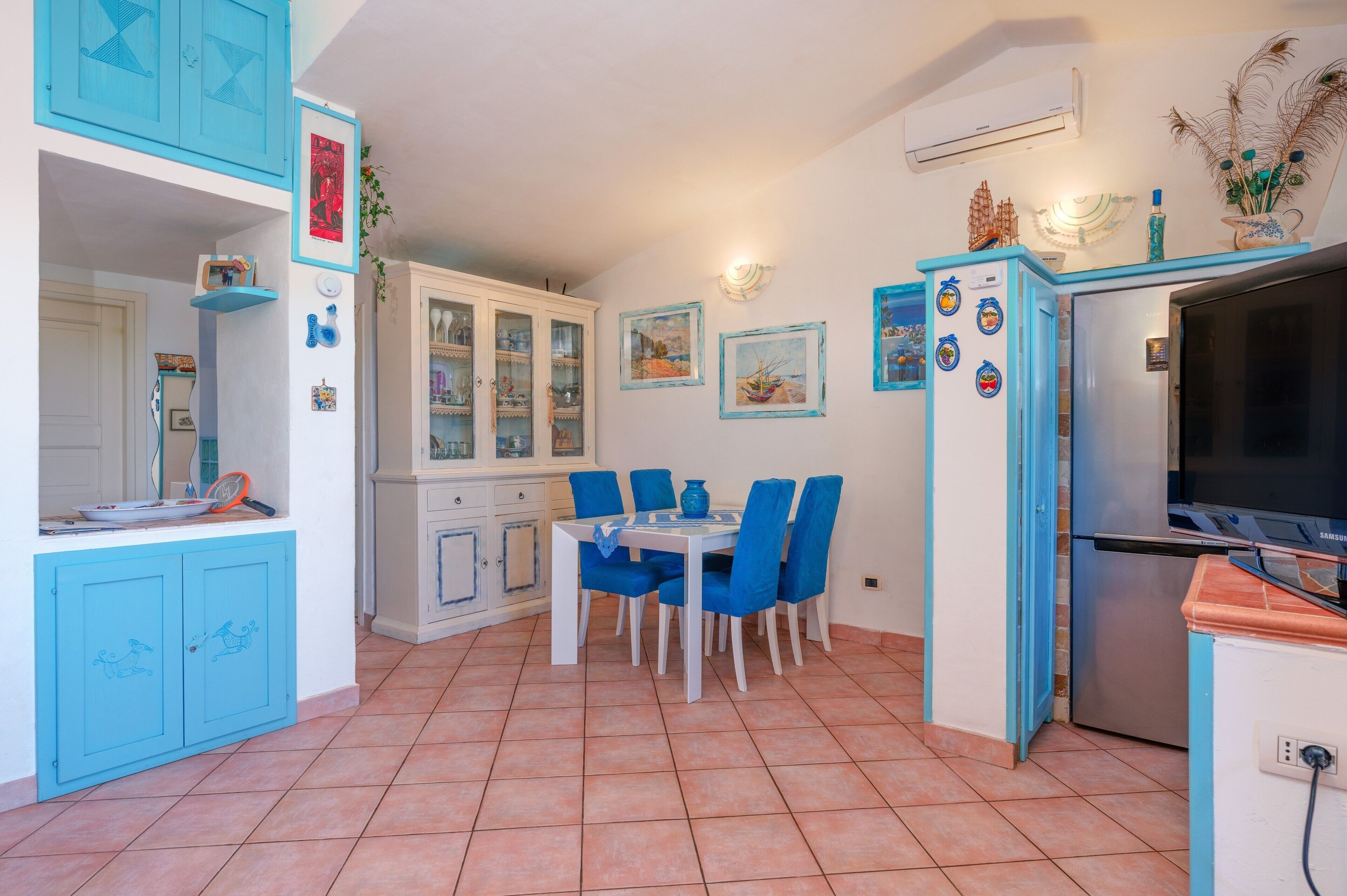 Una cucina con mobili azzurri, un tavolo da pranzo con sedie, un frigorifero e una televisione.