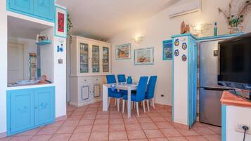 Una cucina con mobili azzurri, un tavolo da pranzo con sedie, un frigorifero e una televisione.