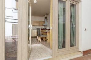 An open sliding door leading to a kitchen with wooden cabinets, a dining table, and a chair.