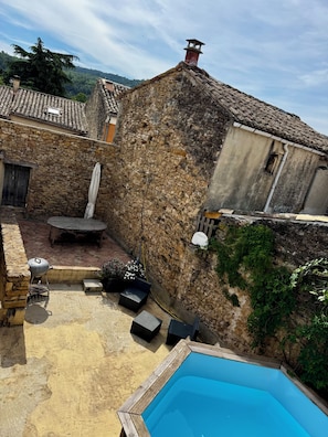 A stone building with a tiled roof, a pool, outdoor furniture, and a garden area.