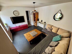 A living room with a TV, red entertainment unit, wooden coffee table, and a sofa with cushions.