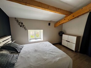 A bedroom with a bed, a window, a fan, and a wardrobe.
