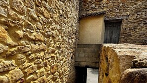 Ein schmaler, gepflasterter Weg führt zu einem Gebäude mit einer Holztür und einer Steinsäule.