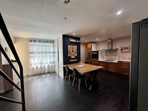 A modern kitchen with a dining area, wooden cabinets, a clock, and a staircase.