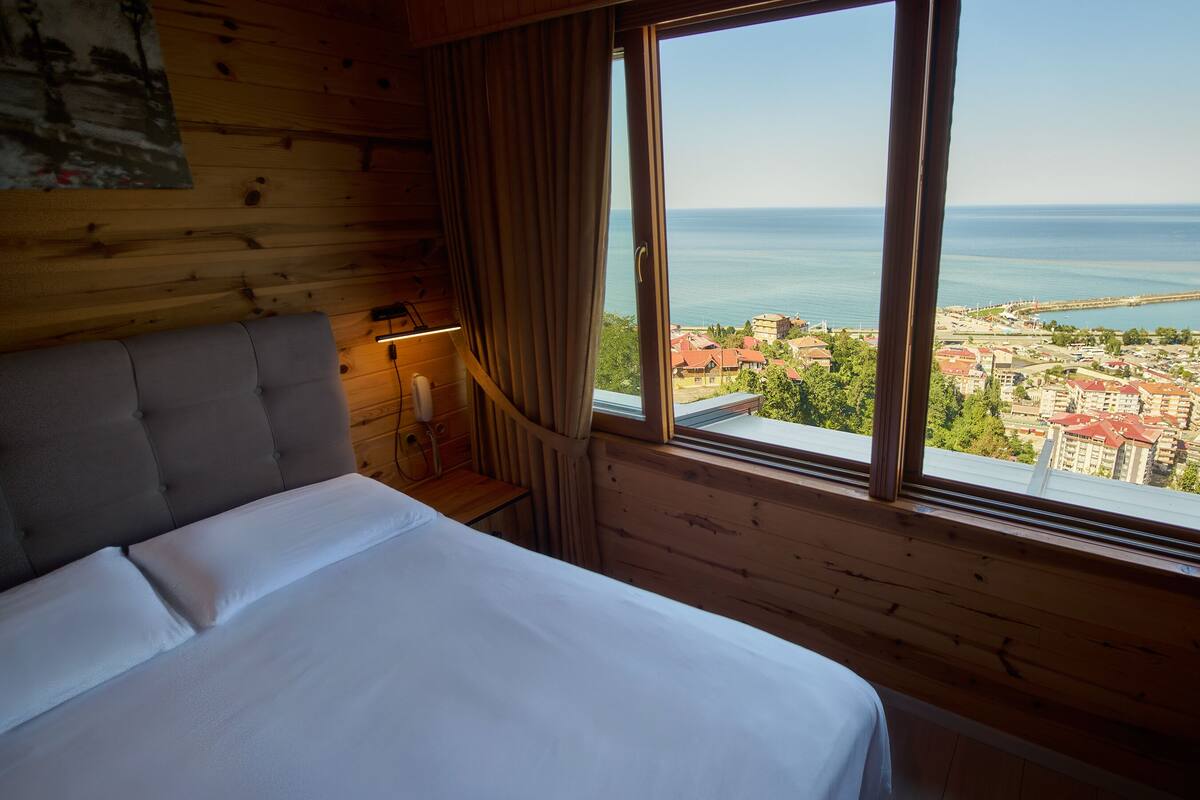 A bedroom with a large window, a bed, a nightstand, and a lamp.