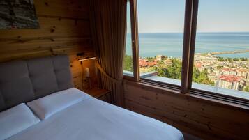 A bedroom with a large window, a bed, a nightstand, and a lamp.