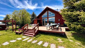 En træhytte med terrasse, udendørs møbler og udsigt til et bjerg.