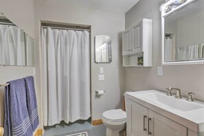 A bathroom with a shower curtain, toilet, sink, and cabinets. - Tasteful Country Home on 5 Acres ~ 3 Mi to Lake! (Westmoreland)