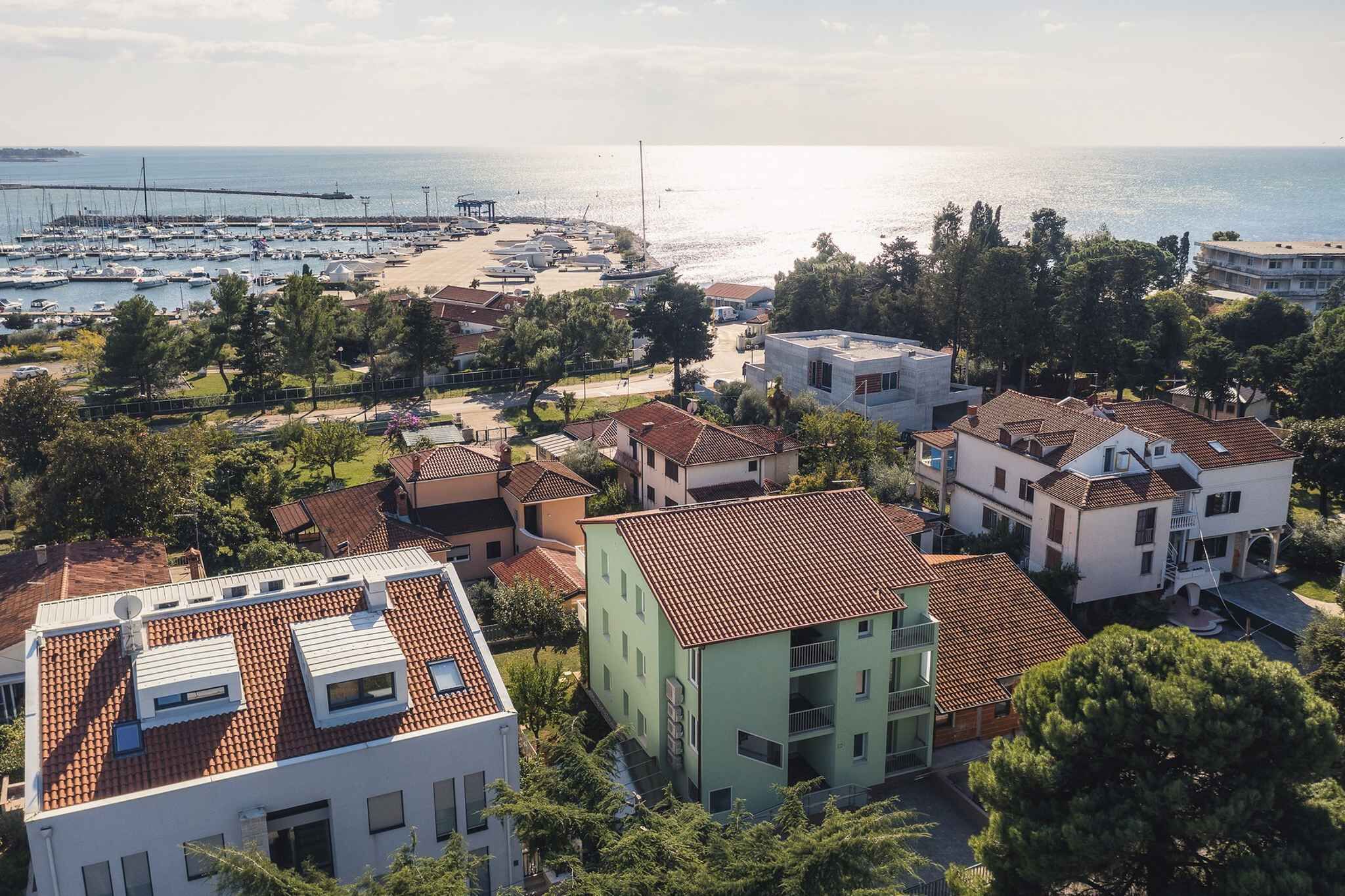 Uma área residencial costeira com um porto de iates, casas com telhados vermelhos e vista clara para o mar.
