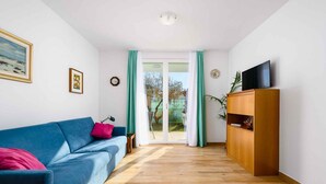 A living room with a blue sofa, a wooden cabinet, and a TV on top. - Holiday apartment with internet and air conditioning near the sea (Umag)