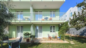 A two-story building with a balcony, a small patio with a table and chairs, and a grassy yard. - Holiday apartment with internet and air conditioning near the sea (Umag)
