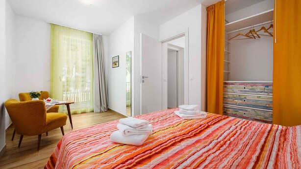 A hotel room with a bed, a chair, a table with a plant, and a wardrobe. - Holiday apartment with internet and air conditioning near the sea (Umag)