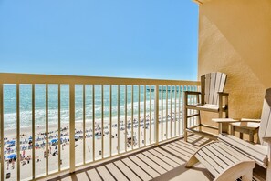 A balcony with a view of a beach, wooden chairs, and a railing.