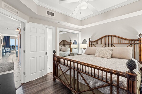 A spacious bedroom with a large bed, a ceiling fan, and a view of the ocean through an open door.
