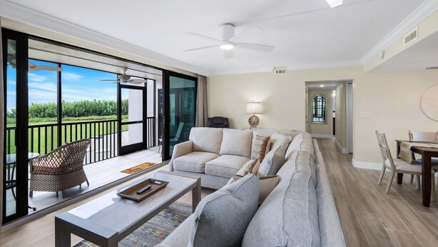 Un vaste espace de vie comprenant un canapé, une table basse et une table à manger, un ventilateur de plafond et une vue sur la verdure grâce à de grandes fenêtres.