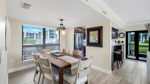 Un coin repas avec une table en bois, des chaises de couleur beige et une vue sur l’extérieur grâce à de grandes fenêtres.