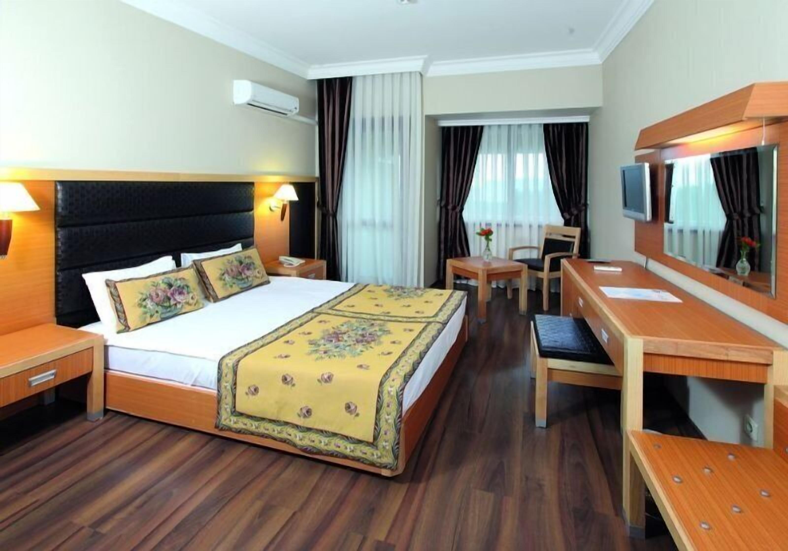 A hotel room with a large bed, a wooden desk, a chair, a TV, and a mirror.