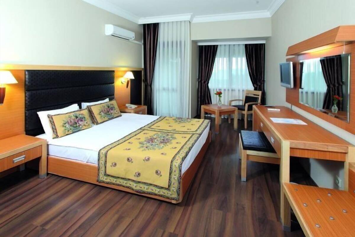 A hotel room with a large bed, a wooden desk, a chair, a TV, and a mirror.