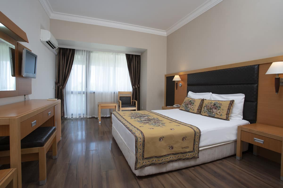 A hotel room with a bed, bedside tables, a desk, a chair, a TV, and curtains.