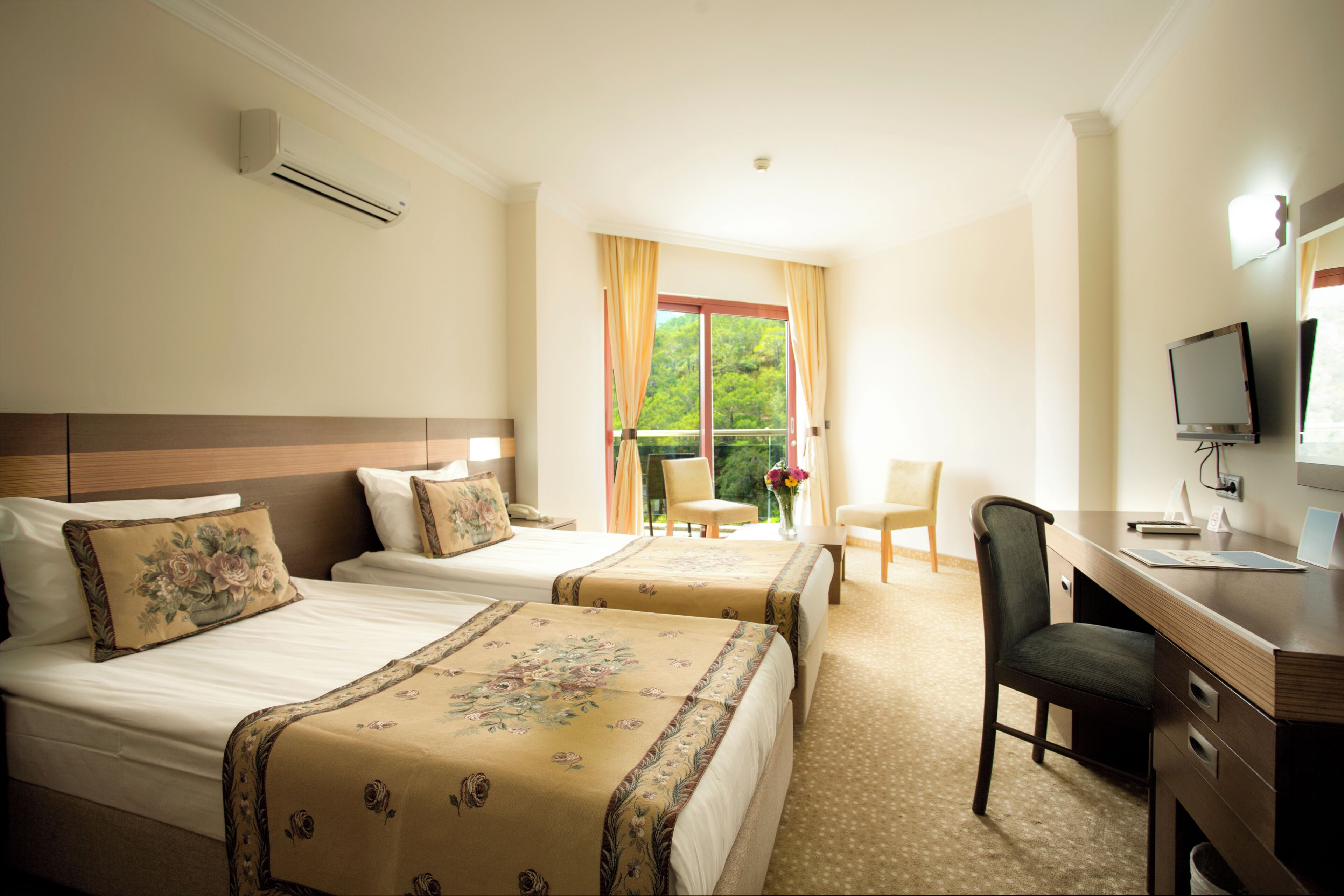 A hotel room with two beds, a desk, a chair, and a TV.