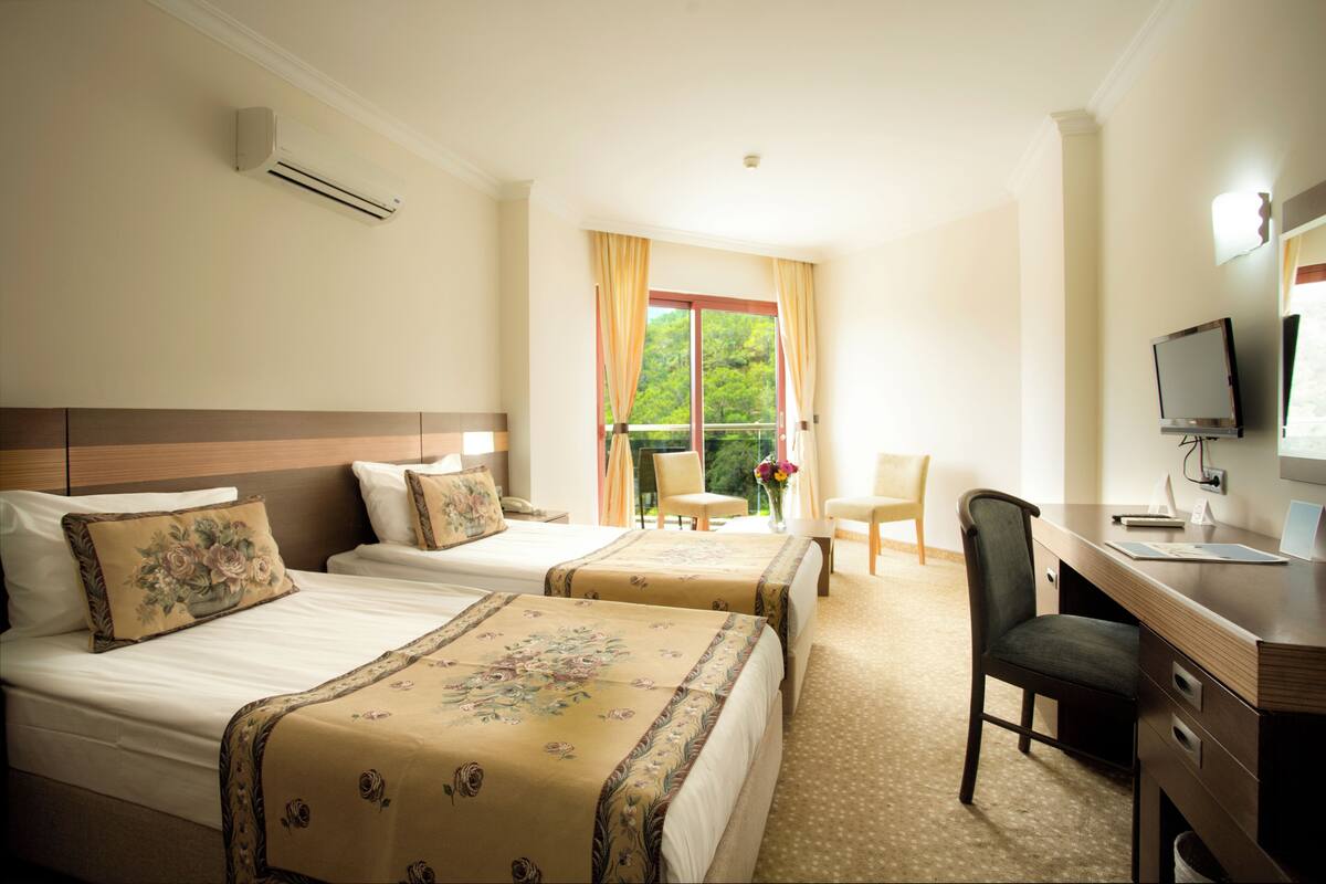 A hotel room with two beds, a desk, a chair, and a TV.