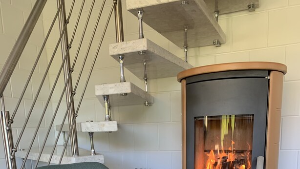Una sala de estar moderna con chimenea de piedra, un sillón verde y una escalera con barandillas metálicas.