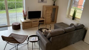 Una sala de estar moderna con un sofá gris, un mueble de madera, un televisor y una mesa de centro de vidrio.