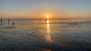 Una playa al atardecer con cielo despejado, agua tranquila y dos personas de pie en la orilla.