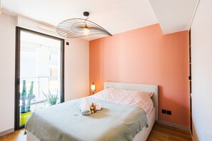 A bedroom with a bed, a nightstand, a lamp, and a view of the outside.